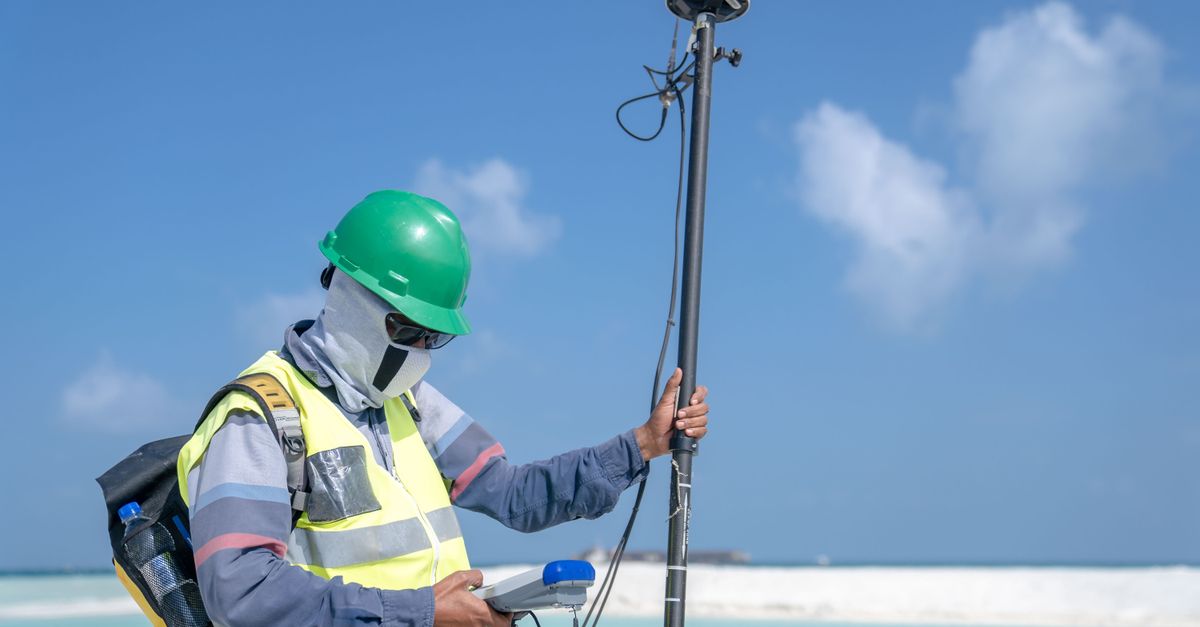 Surveyor using GPS equipment for land measurement outdoors under a clear sky.